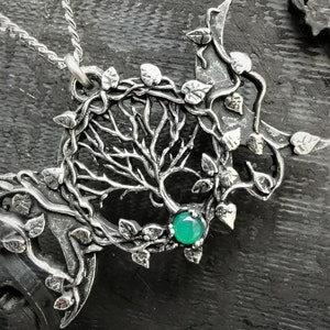 May include: A silver pendant necklace featuring a tree of life design with intricate branches and leaves. The pendant has a green gemstone in the center.