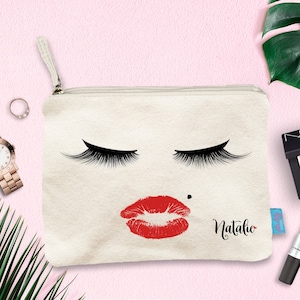 Könnte beinhalten: Eine weiße Canvas-Schminktasche mit einem roten Lippenstift-Druck, schwarzen Wimpern und dem Namen "Natalie" auf der Vorderseite.