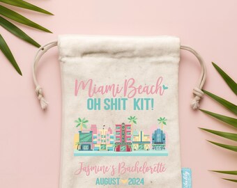 Puede incluir: Una bolsa de lona de color crema con cordón que presenta el texto Miami Beach OH SHIT KIT! en rosa y turquesa, un gráfico colorido del horizonte de Miami con palmeras y el texto Jasmine's Bachelorette AUGUST 2024 en rosa y turquesa.