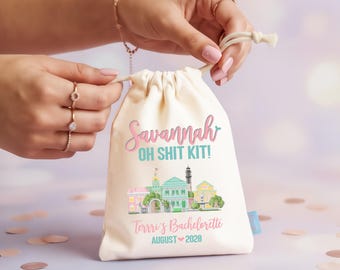 Puede incluir: Una bolsa de color crema con cordón que presenta el texto Savannah OH SHIT KIT! en rosa y turquesa, una ilustración colorida de un horizonte urbano y el texto Terrri's Bachelorette AUGUST 2028 en letras de color rosa y turquesa al frente.
