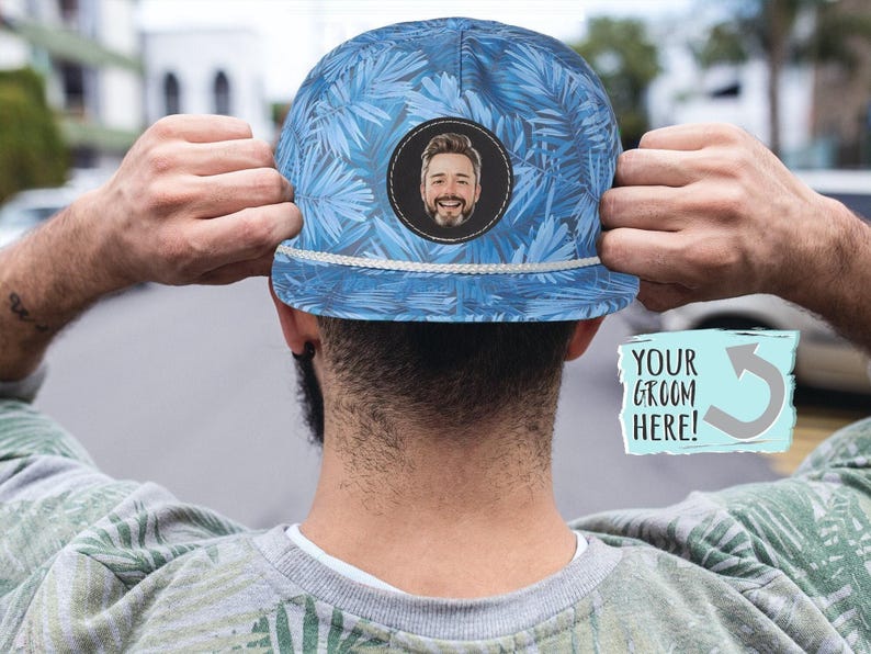 May include: A blue and white patterned baseball cap with a white brim. The cap has a circular cutout with a person's face inside. The text 'YOUR GROOM HERE!' is on a blue and white rectangle with a curved arrow.