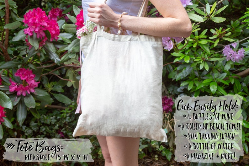 May include: A white canvas tote bag with pink ribbon handles. The bag is 15 inches wide and 16 inches high. The text on the bag reads: "Tote Bags: Measure 15"W x 16"H". The text on the right side of the bag reads: "Can Easily Hold: 4 Bottles of Wine, A Rolled Up Beach Towel, Sun Tanning Lotion, A Bottle of Water, A Magazine + More!"