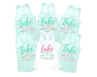 May include: Five light mint green racerback tank tops and one white racerback tank top. The mint tops feature the text "lake LIFE" in teal, a grey oar graphic, and "Jennys Bachelorette LAKE TAHOE" in pink. The white top says "lake WIFE" in pink.