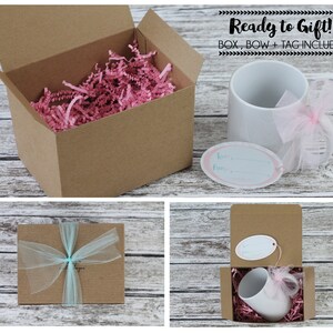 May include: A white ceramic mug with a pink ribbon and a gift tag that says "To my favorite..." is packaged in a brown cardboard box with pink tissue paper. The box is tied with a blue ribbon. The text "Ready to Gift! BOX, BOW + TAG INCLUDED" is displayed above the image.
