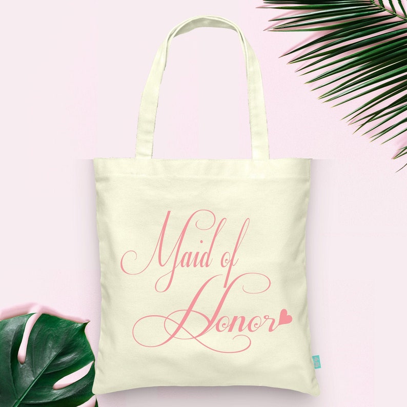 May include: A white canvas tote bag with pink text that says "Maid of Honor" with a small pink heart.