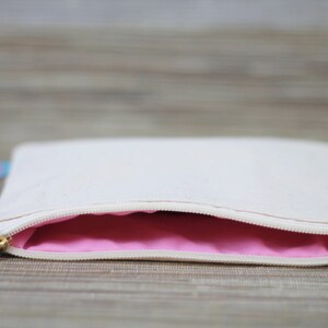 May include: A white canvas zippered pouch with a pink lining. The pouch is open and the zipper is visible.