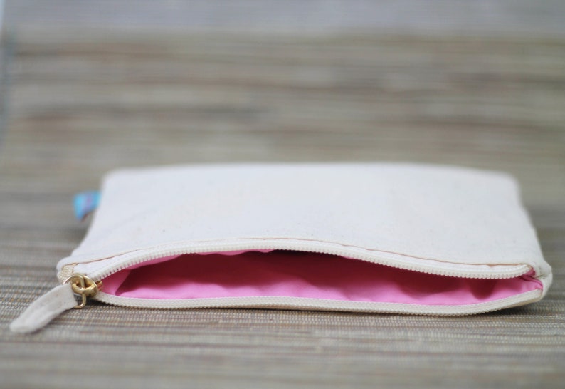 May include: A white canvas zippered pouch with a pink lining. The pouch is open and the zipper is visible.