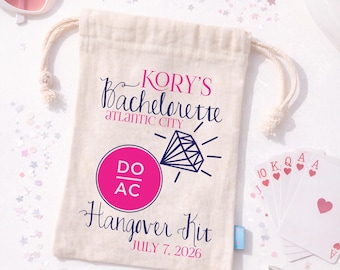 May include: A beige drawstring canvas pouch featuring the text KORY'S Bachelorette ATLANTIC CITY, a diamond graphic, a pink circle with DO AC, and the text Hangover Kit JULY 7, 2026. The pouch is surrounded by heart-shaped sunglasses and playing cards.
