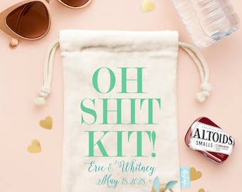 May include: A cream-coloured fabric drawstring pouch with the teal text "OH SHIT KIT!" printed on the front, along with the names "Eric & Whitney" and the date "May 18, 2028". The pouch is surrounded by sunglasses, a water bottle, and mints.