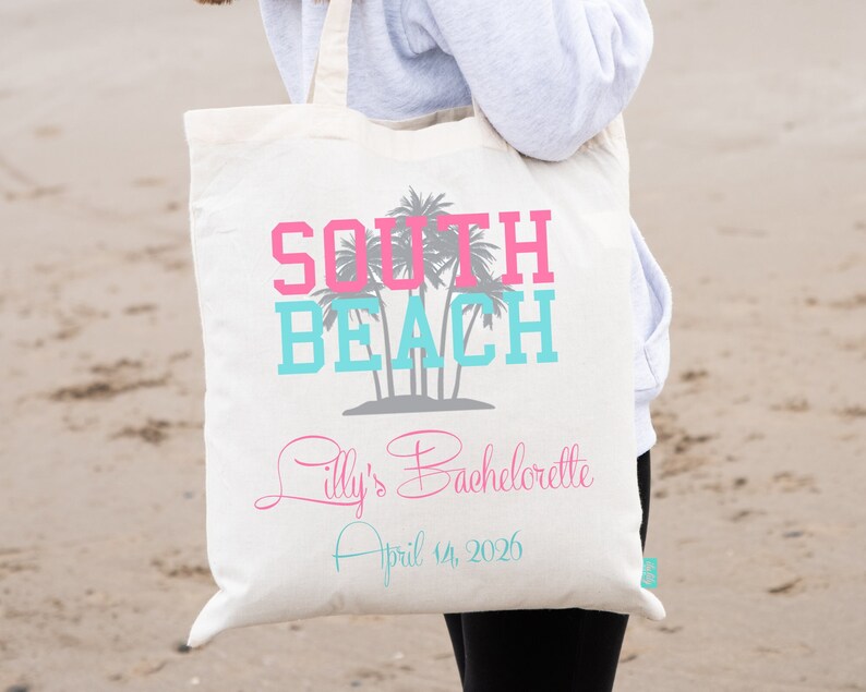 May include: White canvas tote bag with the text "South Beach" in pink and blue lettering. The bag also has a palm tree graphic and the text "Lilly's Bachelorette April 14, 2026" in pink and blue lettering.