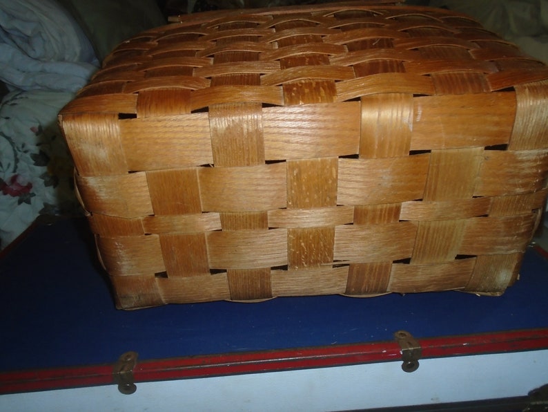 Puede incluir: Una cesta de mimbre de madera de color marr&oacute;n claro. La cesta est&aacute; hecha de finas tiras de madera que se tejen juntas para crear un recipiente resistente y duradero.