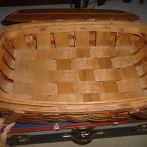 Puede incluir: Una cesta de picnic de madera vintage con un interior tejido y una tapa de cuero. La cesta est&aacute; vac&iacute;a y lista para un picnic.
