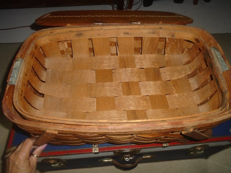Puede incluir: Una cesta de picnic de madera vintage con un interior tejido y una tapa de cuero. La cesta est&aacute; vac&iacute;a y lista para un picnic.
