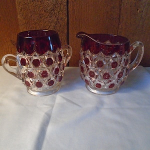 May include: A set of two clear glass sugar and creamer with a ruby red overlay and a diamond pattern.