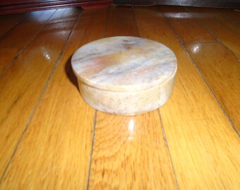 May include: A round, light brown stone trinket box with a lid. The box has a swirling pattern of light and dark brown.