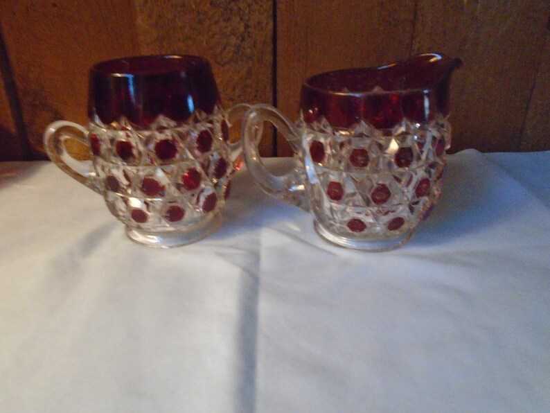 May include: A vintage set of a red glass creamer and sugar bowl with a diamond pattern and red accents.