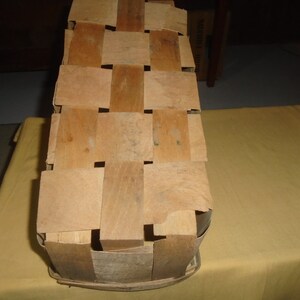 K&ouml;nnte beinhalten: Ein geflochtener Holzkorb mit rechteckiger Form und hellbrauner Farbe. Der Korb besteht aus d&uuml;nnen Holzstreifen, die miteinander verflochten sind, um ein Gittermuster zu erzeugen.