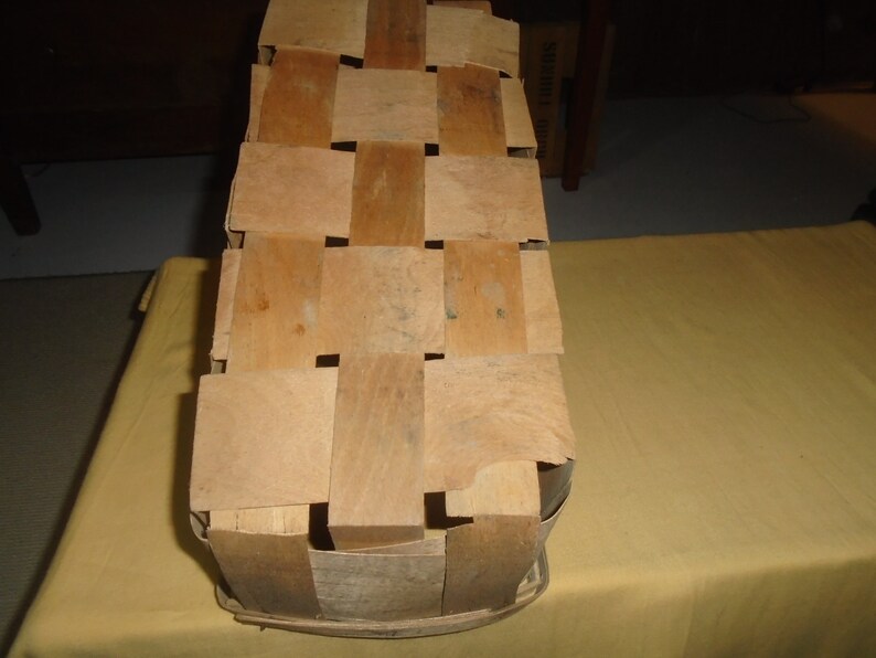 K&ouml;nnte beinhalten: Ein geflochtener Holzkorb mit rechteckiger Form und hellbrauner Farbe. Der Korb besteht aus d&uuml;nnen Holzstreifen, die miteinander verflochten sind, um ein Gittermuster zu erzeugen.