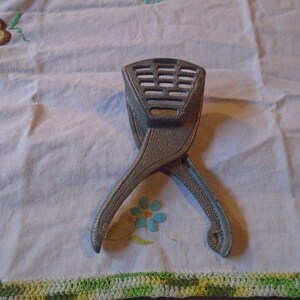 May include: A silver metal citrus juicer with a textured surface and a gridded top. The juicer is open and ready to use.