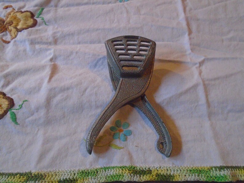 May include: A silver metal citrus juicer with a textured surface and a gridded top. The juicer is open and ready to use.
