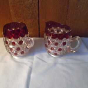 May include: A set of two clear glass creamer and sugar bowls with a red, diamond-shaped pattern.