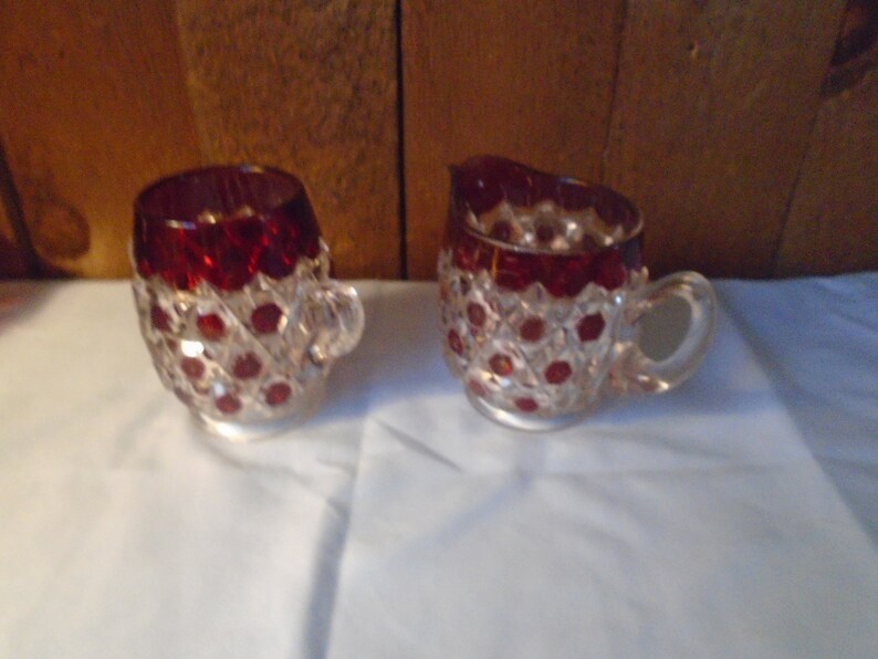 May include: A set of two clear glass creamer and sugar bowls with a red, diamond-shaped pattern.