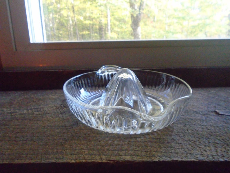 May include: A clear glass citrus juicer with a ribbed design. The juicer has a central cone with three sections for squeezing citrus fruits.