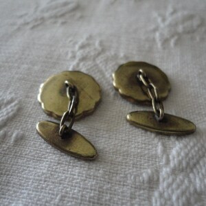 May include: A pair of gold cufflinks with a chain connecting them. The cufflinks have a round design with a textured surface.