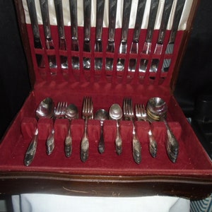 May include: A wooden box with a red velvet interior containing a set of silver flatware. The flatware includes forks, knives, and spoons.