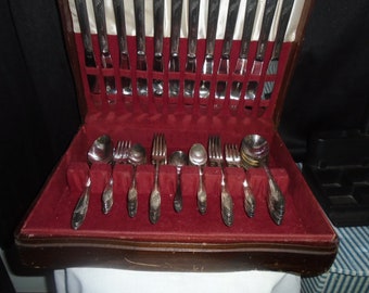 May include: A wooden box with a red velvet interior containing a set of silver flatware. The flatware includes forks, knives, and spoons.