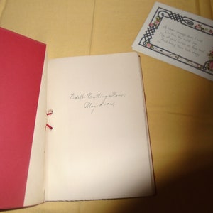 May include: An open book with a red cover and a white page. The page has a handwritten inscription that reads "Edith Cutting Jones, May 9, 1904".