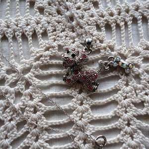 Pu&ograve; includere: Una collana con catena d'argento con un ciondolo a forma di cane in strass rosa e un ciondolo a forma di osso in strass abbinato.