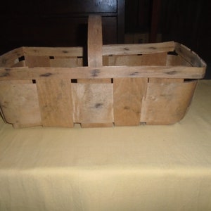 K&ouml;nnte beinhalten: Ein Holzkorb mit einem Griff, aus geflochtenen Latten. Der Korb ist leer und hat eine nat&uuml;rliche Holzfarbe.