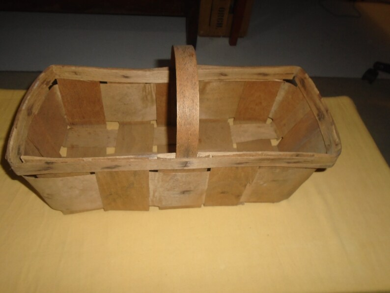 K&ouml;nnte beinhalten: Ein Korb aus Holz mit geflochtenem Muster und einem einzelnen Griff. Der Korb ist leer und hat eine nat&uuml;rliche Holzoptik.