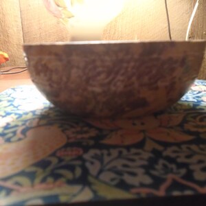 May include: A brown, textured bowl with a floral pattern. The bowl is set on a blue and orange patterned surface. The bowl's exterior has a detailed, carved design.