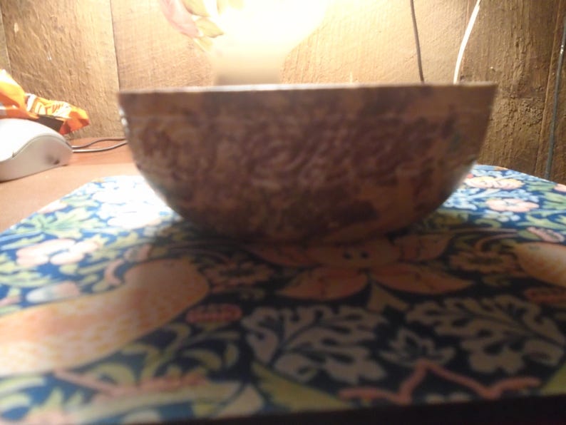 May include: A brown, textured bowl with a floral pattern. The bowl is set on a blue and orange patterned surface. The bowl's exterior has a detailed, carved design.