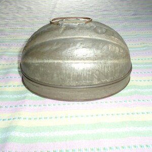 May include: A vintage metal mold for making a dome-shaped cake or dessert. The mold is silver in color and has a ribbed design. It has a handle on the top.