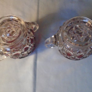 May include: Two clear glass cream jugs with a red, star-shaped pattern. The jugs have a round, clear glass top with a star-shaped design.