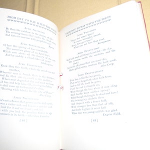 May include: An open book with a red spine and white pages. The book is titled "From Day to Day with the Poets" and features poems about the month of April. The text is in black ink and the pages are slightly yellowed.