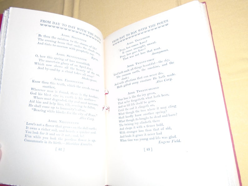 May include: An open book with a red spine and white pages. The book is titled "From Day to Day with the Poets" and features poems about the month of April. The text is in black ink and the pages are slightly yellowed.