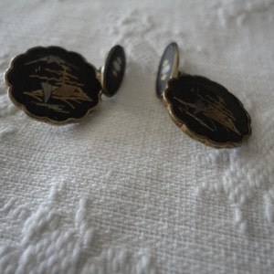 May include: A pair of gold cufflinks with black enamel and a gold and white design. The design features a stylized bird in flight.