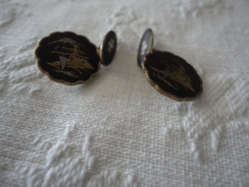 May include: A pair of gold cufflinks with black enamel and a gold and white design. The design features a stylized bird in flight.