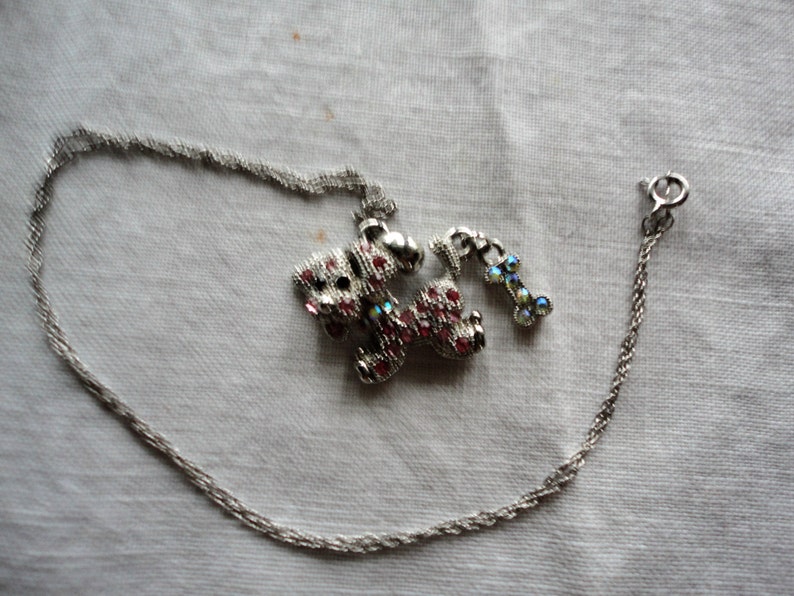 Pu&ograve; includere: Una collana a catena d'argento con un ciondolo a forma di cane rosa e argento con strass e un ciondolo separato a forma di osso d'argento con strass.
