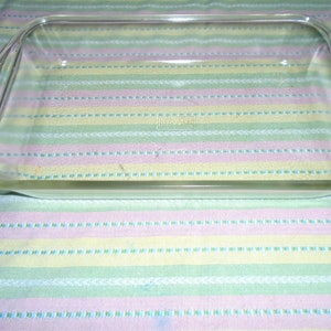 May include: A clear glass baking dish with two handles. The dish is empty and sitting on a striped fabric.