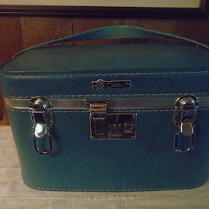 May include: Teal vintage train case with a handle, silver trim, and a combination lock. The case has a textured surface and white stitching. The brand name "JS Mellor" is displayed on a silver plaque.