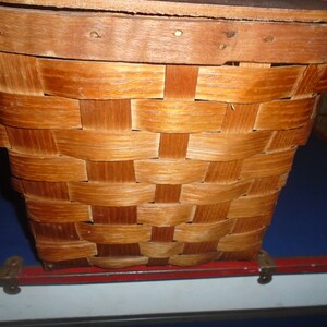 Puede incluir: Una cesta de mimbre de madera con un acabado marr&oacute;n natural. La cesta tiene una forma rectangular y est&aacute; hecha de finas tiras de madera que se entrelazan.