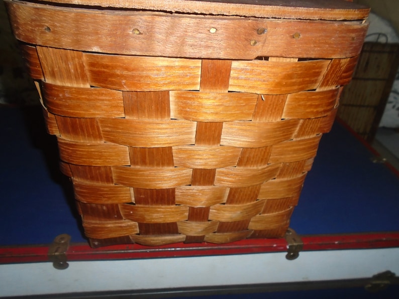 Puede incluir: Una cesta de mimbre de madera con un acabado marr&oacute;n natural. La cesta tiene una forma rectangular y est&aacute; hecha de finas tiras de madera que se entrelazan.