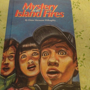 May include: A book cover with the title "Mystery of the Island Fires" by Elaine Macmann Willoughby. The cover features three children with surprised expressions, two girls and a boy wearing a baseball cap.