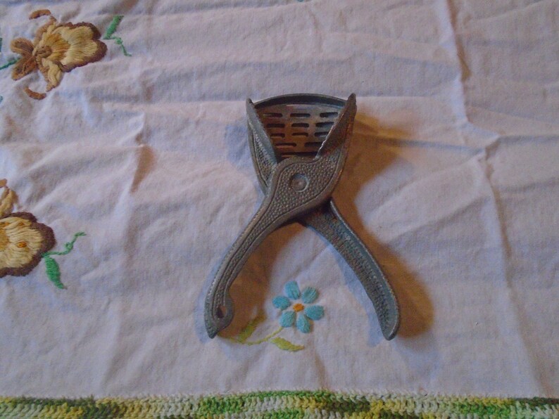 May include: A vintage silver-colored citrus juicer with a criss-cross design. The juicer is open and ready to use.