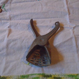 May include: A vintage metal citrus juicer with a handle and a gridded base. The juicer is silver in color and has a worn, rustic look.